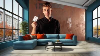 Close-up portrait of young man with gambling cards. Handsome guy shows tricks with card. Clever hands of magician on metal texture background. Concept of entertainment and Hobbies. Copy space Wall mural