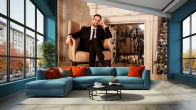 Young businessman man in suit is sitting on chair in living room holding hand on his head. Gesture of person indicates calmness, relaxation and home comfort. Concept of human emotions. Copy space Wall mural