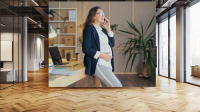 Beautiful Young Pregnant Woman at Work in a Comfortable Modern Office. A Happy, Attractive, Pensive Office Worker at the Workplace. Motherhood, Work, and Comfort. Wall mural