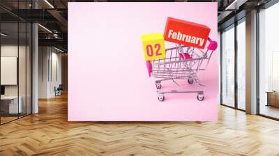 February 2nd. Day 2 of month, Calendar date. Close up toy metal shopping cart with red and yellow box inside with Calendar date on pink background. Winter month, day of the year concept. Wall mural