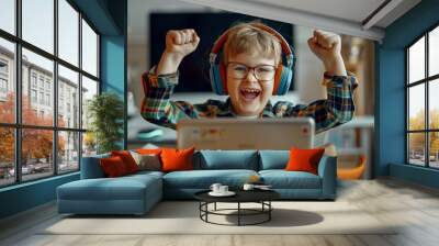 A child wearing glasses and headphones is celebrating victory on a laptop Wall mural