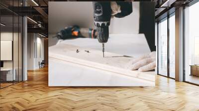 A man holds a cordless screwdriver in his hand and wraps the screw in a Board. Wall mural