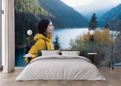 A young female tourist in a yellow hoodie goes hiking with a backpack on her back Wall mural