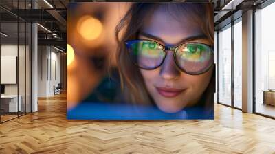 Beautiful young woman wearing glasses looking at laptop at night Wall mural