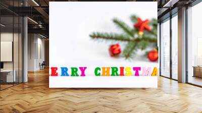 Creative layout of words merry christmas made of wooden multi-colored letters on white background with blurred fir branch and red toys. New Year concept with copy space for note and text Wall mural