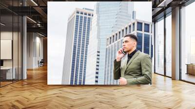 Young American Businessman traveling, working in New York, standing in front of business district with high buildings, looking away, calling on cell phone.. Wall mural