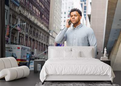 Young Mix Race American Businessman talking on cell phone, traveling in New York City, wearing gray shirt, carrying laptop computer, walking on street in Manhattan. Cars, buildings on background.. Wall mural