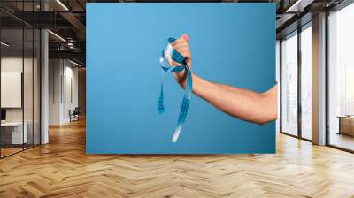 Lose weight, get rid of excess weight, a call to engage in health. A man's hand holds a centimeter ribbon in his fist, blue background Wall mural