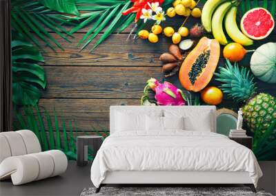 Assortment of tropical fruits with leaves of palm trees and exotic plants on dark wooden background Wall mural