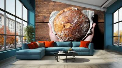 Baker's hands holding and presenting fresh baked loaf of bread Wall mural