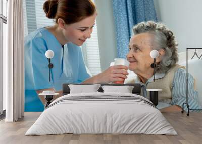 Nurse cares for a elderly woman lying in bed Wall mural