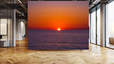 The sun is sinking below the horizon over the sea Wall mural