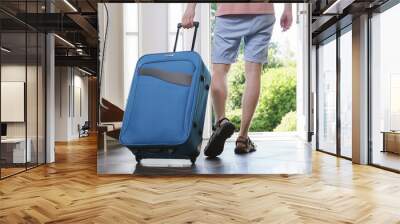 Tourist young man in T-shirt, shorts and sandals with blue vacation bag exits through the front door. Wall mural