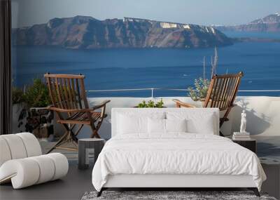 Two chairs on a balcony in the town of oia on make up a tranquil scene with the island of background Wall mural