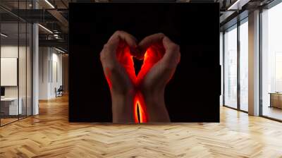 Two hands folded in the shape of a heart, light inside. Clench your hands, symbol of love. Black background Wall mural