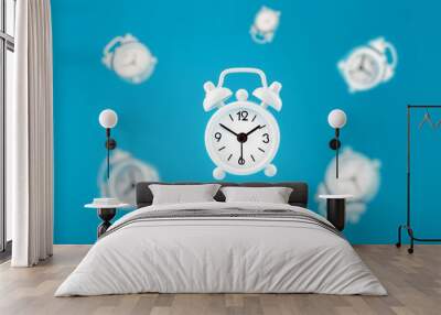 White retro alarm clocks in flight in the center, isolated on a blue background.Creative modern still life concept of flying time. Wall mural