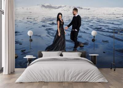 Young beautiful wedding couple in black clothes stands  backdrop of mountains in Iceland Wall mural