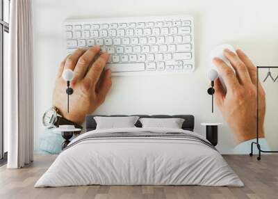 Man is holding his hands on the white computer keyboard and mouse. Flat lay of the white minimalists working place Wall mural