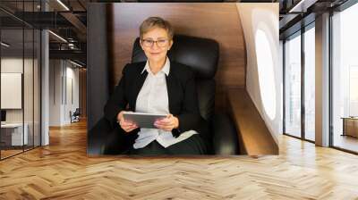 beautiful aged woman in the cabin of a private plane in a chair with a tablet in her hands Wall mural