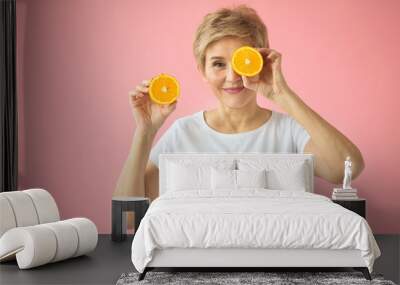 beautiful elderly woman in a white T-shirt with an orange in her hands on a pink background Wall mural