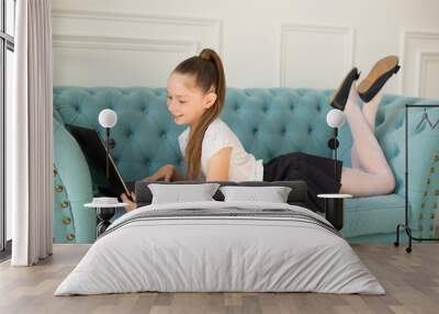 beautiful little teenager girl in a white shirt lies on a sofa with a laptop Wall mural