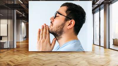 close up of a calm spiritual handsome american guy with glasess praying with closed eyes. side view of a serious peaceful young man with joining hands meditating. Belief concept Wall mural