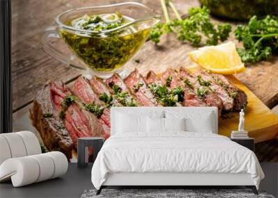 Appetizing beef steak cooked and sliced on a wooden table with chimichurri sauce. Wall mural