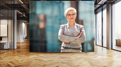 stylish adult woman in age in a suit and glasses against the background of a glass building Wall mural