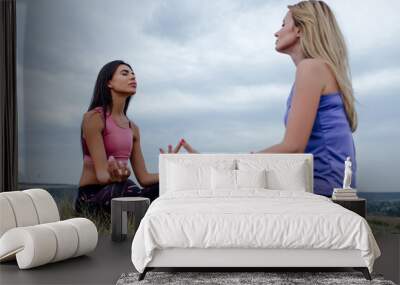 two caucasian woman, doing yoga asana, Young Female wearing sport clothes in lotus pose with sky background. Wall mural