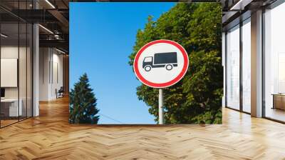 Red and white round traffic sign with black cargo truck indicating No entry for trucks with trees and blue sky on the background Wall mural