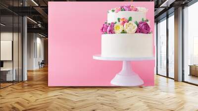 Two-tiered white wedding cake decorated with color cream flowers on a pink background. Wall mural