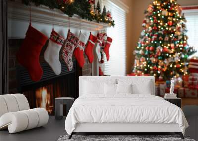 Christmas stockings are hanging from the fireplace mantel with a lit christmas tree in the background Wall mural