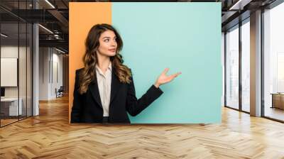 Confident businesswoman in a suit gestures with an open hand against a split orange and teal background, suggesting a presentation or the introduction of an idea or product Wall mural