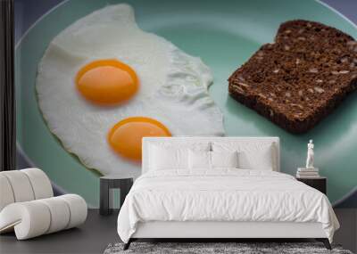 delicious breakfast two fried eggs  with bright yellow yolks on a green plate with a piece of black cereal bread Wall mural