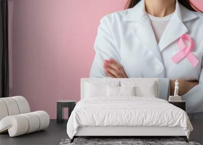 Doctor with crossed arms wearing pink ribbon on white coat against pink background Wall mural