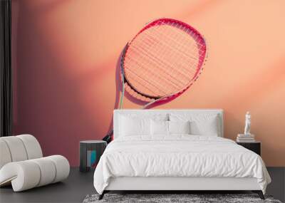 Elevated view of a tennis racket casting shadow on a vivid coral surface, symbolizing active sports lifestyle and equipment Wall mural