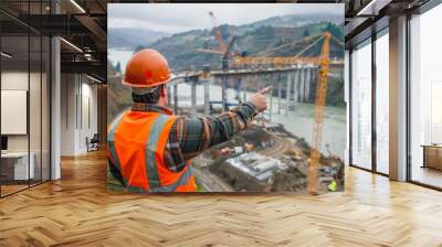 focused construction supervisor in safety gear points ahead while monitoring progress at a bridge co Wall mural