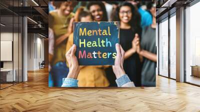 Hands holding a sign reading mental health matters with a diverse group of people clapping in the background Wall mural