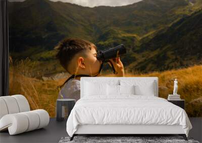 kid in mountains watching with binoculars.beautiful breathtaking landscape with hills and grass.child boy against lake.summer time,vacation mood.preschooler is traveling by car with parents. Wall mural