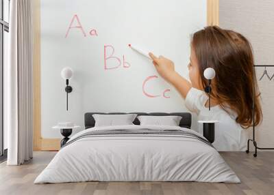 Little pretty girl standing in front of blackboard. She holds a marker and teaches the alphabet. Wall mural