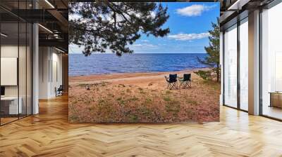 Sunny beach day with two camping chairs overlooking a calm lake under a clear blue sky Wall mural