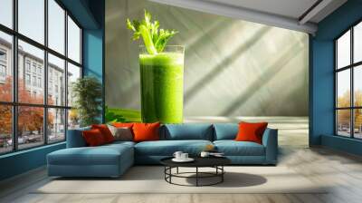 Vibrant green celery smoothie in a clear glass, with fresh celery stalks beside it, bathed in natural sunlight shadows Wall mural