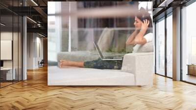 Woman, headphones and a laptop for internet on a home sofa while listening to music or streaming audio. Female student relax on couch to listen to radio channel, podcast or learn language online Wall mural