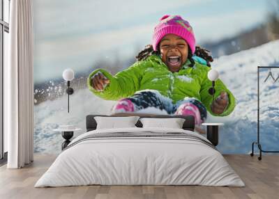 Young girl is having a blast as she sleds down a snow covered hill Wall mural