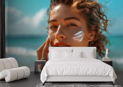 Young woman applying high spf sun cream to her cheek on a sunny beach with clear blue sky in the background Wall mural