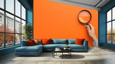 A hand holding a magnifying glass over a orange background with copy space, the concept of searching for information or finding a job candidate	
 Wall mural