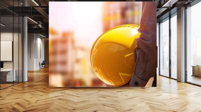 close-up image of a construction worker dressed in safety gear, holding a yellow hard hat securely Wall mural