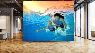 Happy family, mother and daughter, play sports on vacation and swim underwater in the pool in striped swimsuits on a bright Sunny day. They look at the camera and smile. Portrait. Bottom view Wall mural