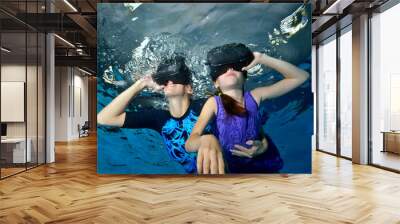 Happy little girl in purple dress and mom are swimming in virtual reality glasses on head underwater in pool on blue background. Bottom view. Close up. Shooting underwater Wall mural