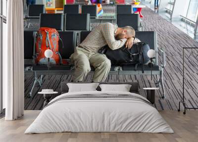 Airport lounge and people waiting for boarding.
Body of male on foreground sleeping on his luggage lying in chair other people miscellaneous actions on background terminal interior with large windows Wall mural